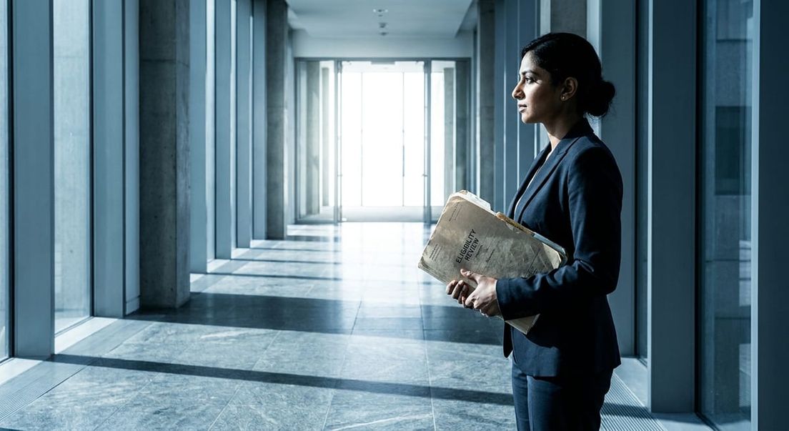 Photograph of a woman in a suit holding an eligibility review folder in a bright hallway for a refugee appeal.