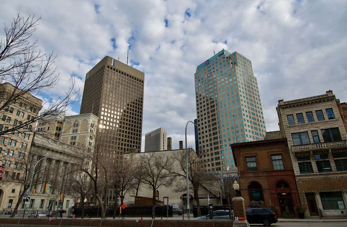 Tall office towers and historic buildings along a downtown street under a partly cloudy sky.