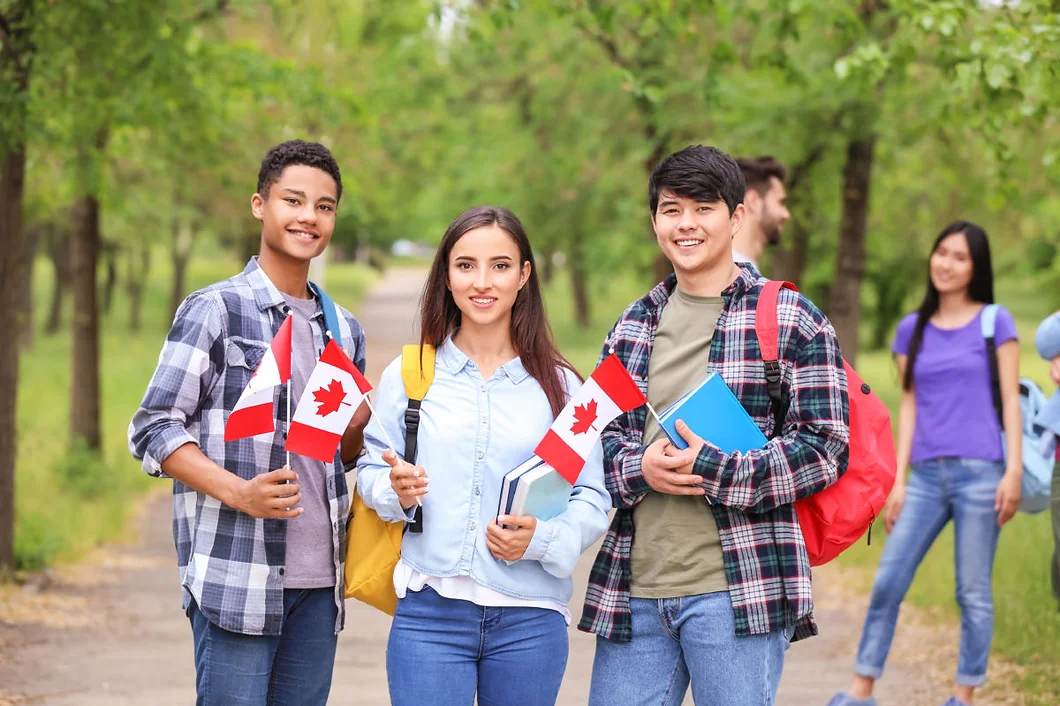 three Canadian students standing side by side and each holding a Canadian flag