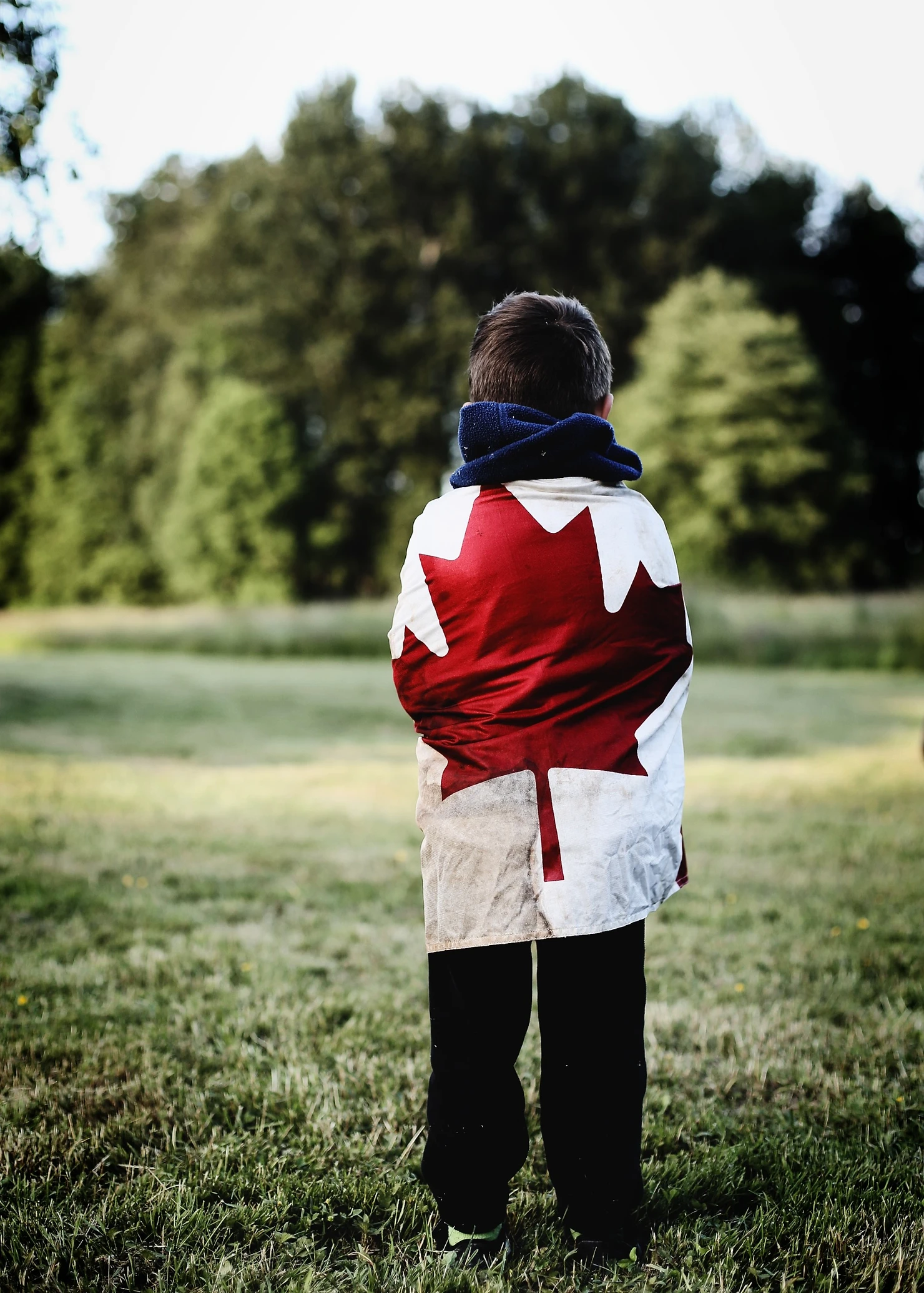 a girl, standing in the middle of woods with the Canadian flag wrapped around her