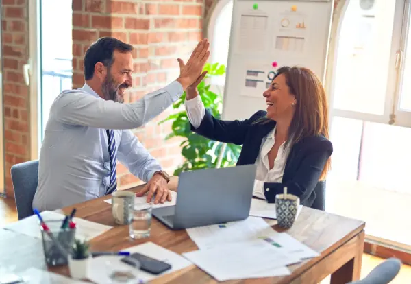 a middle-aged lady and man high-fiving behind a desk