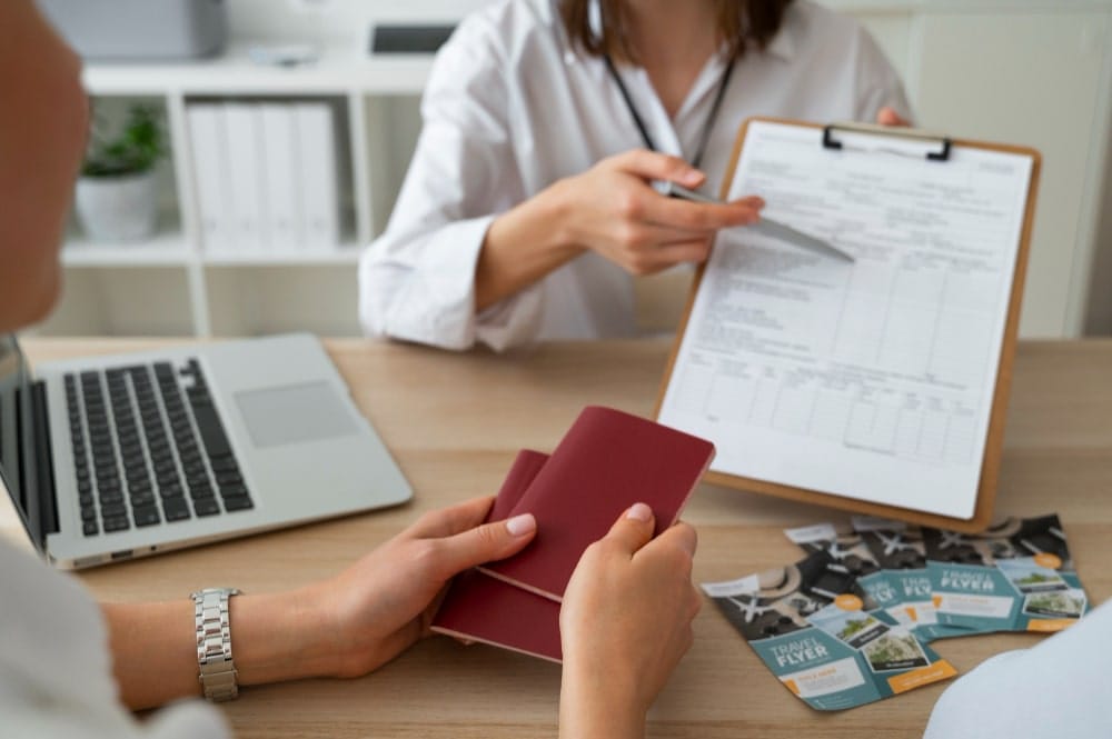 "Close-up of hands exchanging a passport and boarding pass at a travel office, with a laptop and globe in the background.