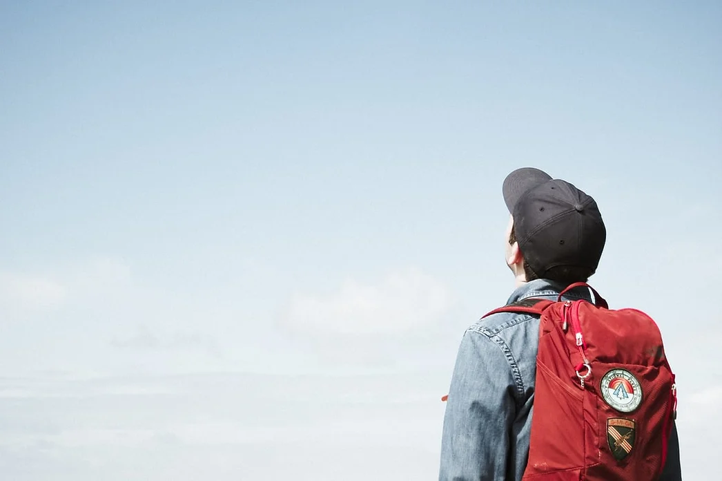 a student with a backpack on, staring at the blue sky