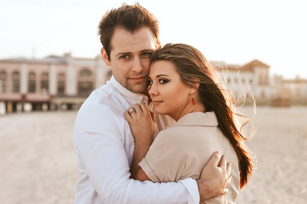 a man dressed in white, holding a woman with long hair on the beach