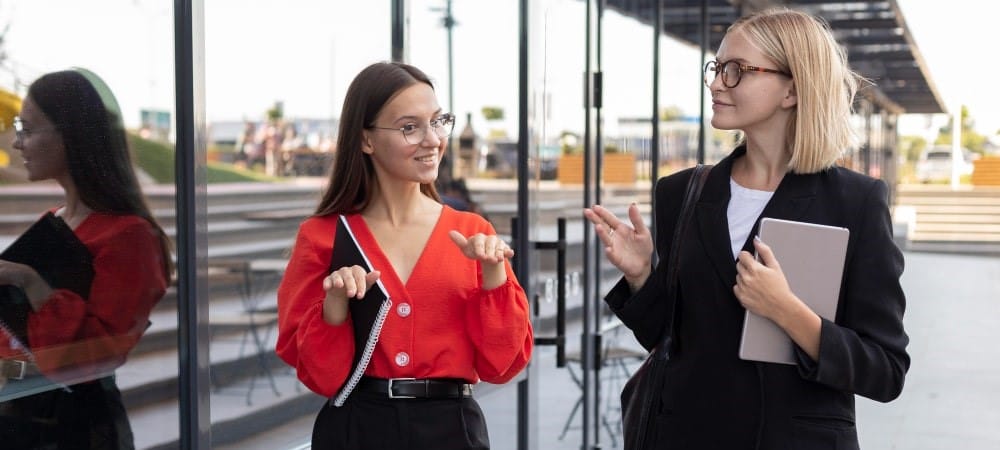 Two businesswomen chatting outside a modern glass building.