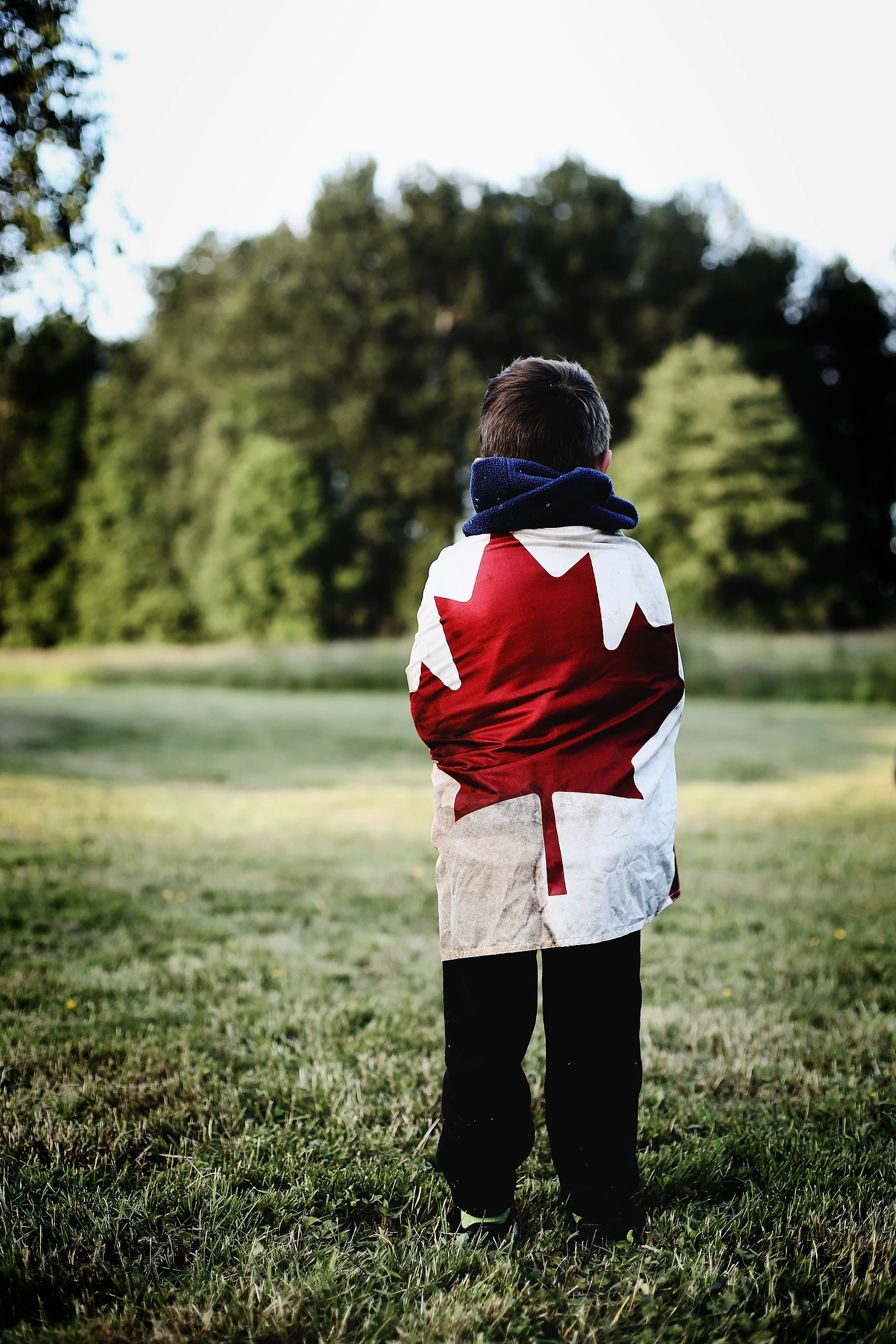 a girl, standing in the middle of woods with the Canadian flag wrapped around her