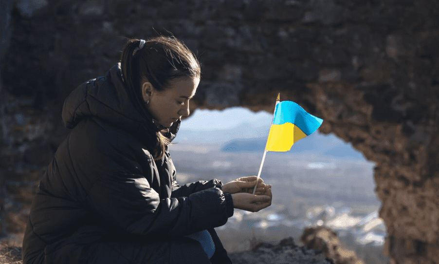 Woman holding a small Ukrainian flag in front of a stone arch.