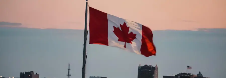 the Canadian flag in front of a sunset with the city being shown behind it