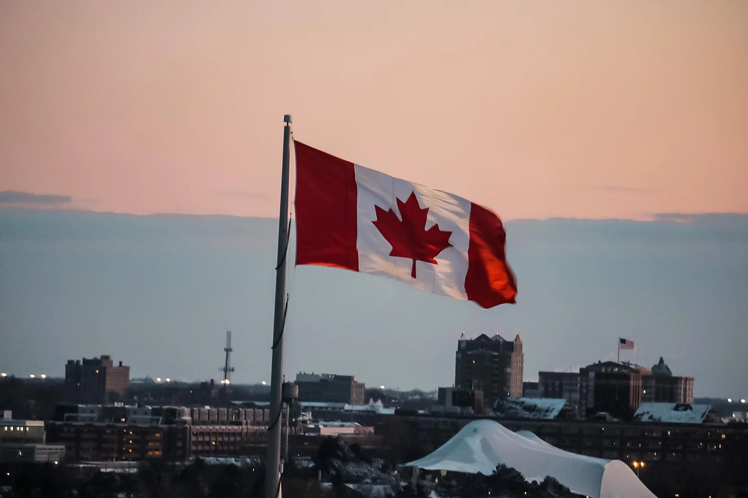 the Canadian flag in front of a sunset with the city being shown behind it