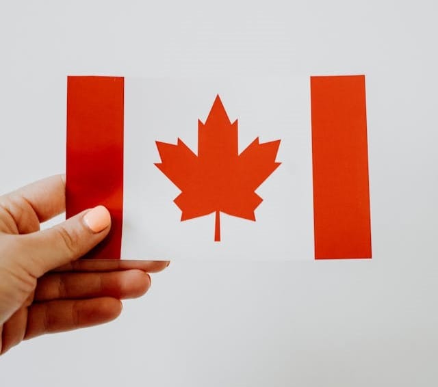 Hand holding a small Canadian flag card against a plain background.