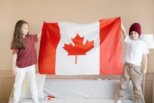 Two children holding a large Canadian flag indoors.