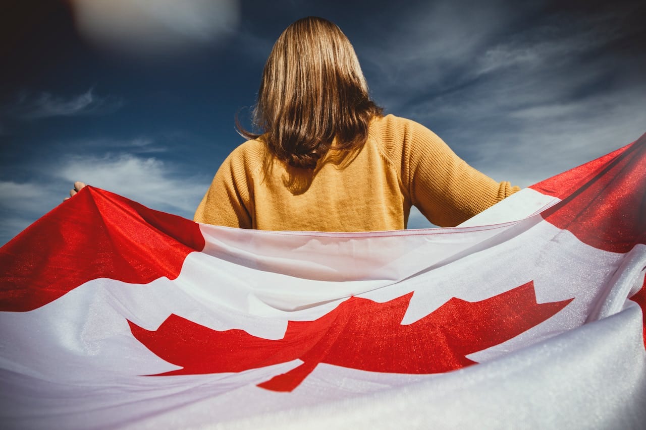 Woman holding a Canadian flag behind her under a dramatic sky.