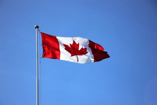 Canadian flag waving on a flagpole against a clear blue sky.