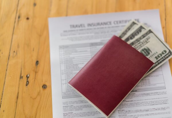 Passport with dollars on top of a travel insurance certificate.