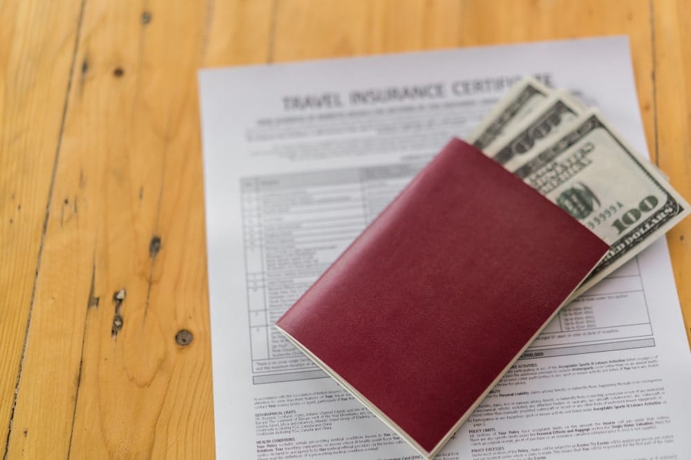 Passport with dollars on top of a travel insurance certificate.