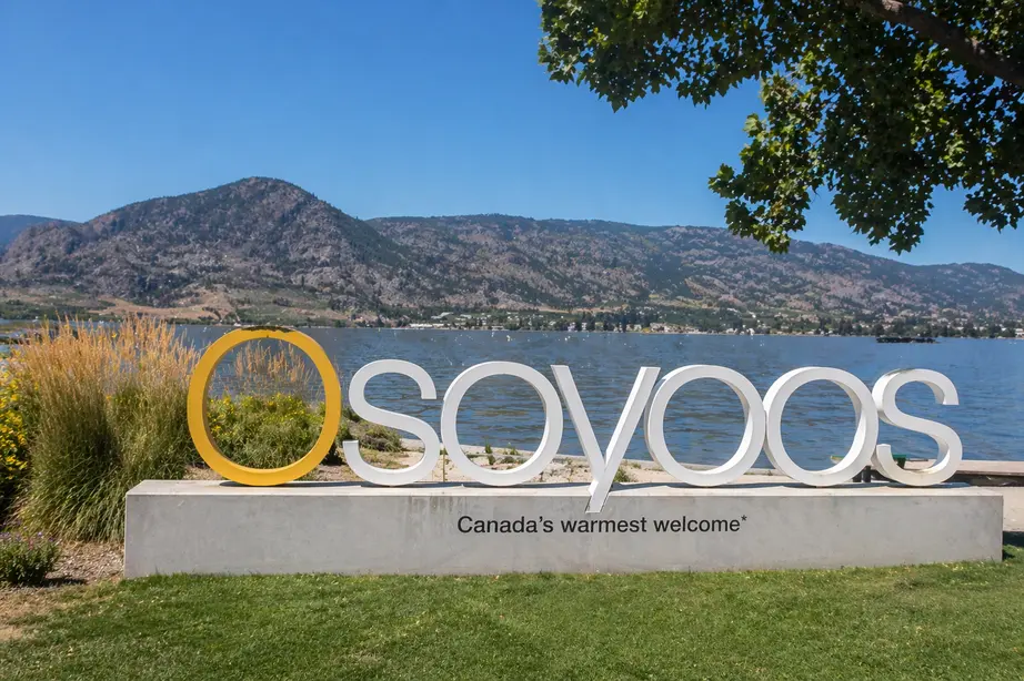 “Waterfront view of Osoyoos sign beside Osoyoos Lake with mountains in the background on a sunny day”