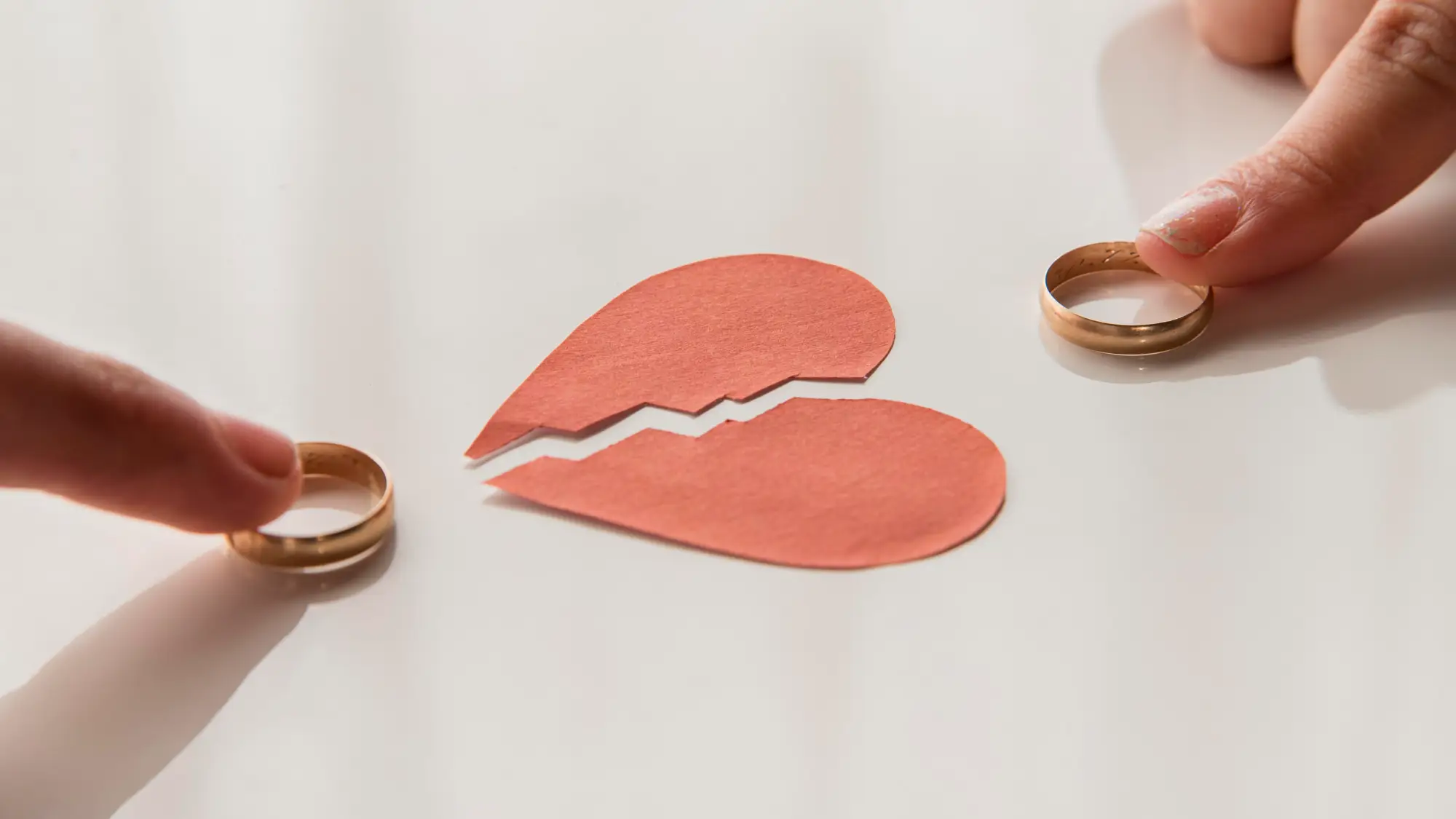 Two hands holding wedding rings on either side of a broken paper heart, symbolizing divorce or separation affecting Canadian sponsorship commitments