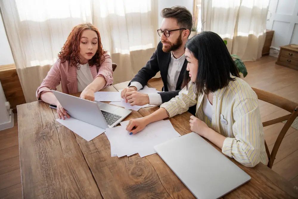 Three people discussing documents and strategies for Canadian spousal sponsorship interview preparation